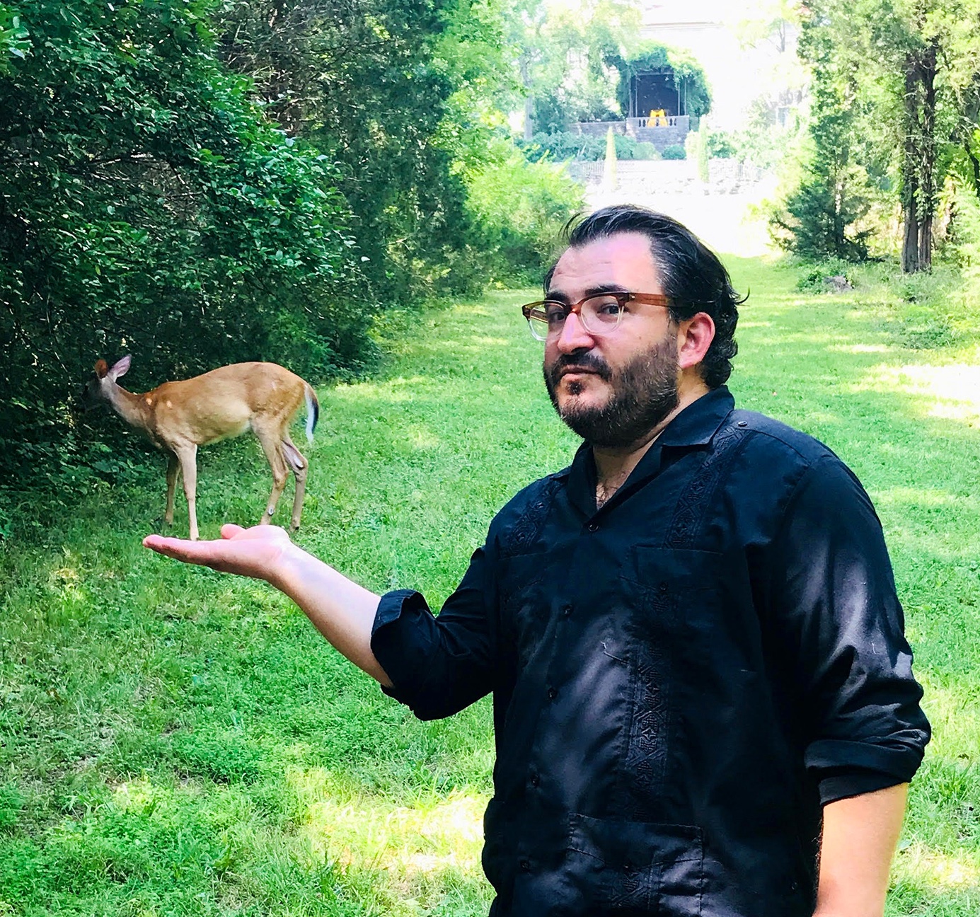 A photo of David foregrounding a deer with his palm out appearing to be holding a the deer.